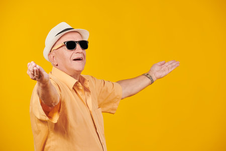 Portrait of an old elegant man in summer clothes and sunglasses standing joyfully with outstretched...