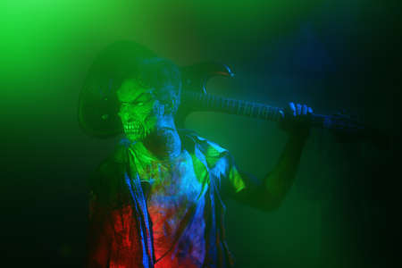 A scary zombie man holds an electric guitar while standing in a cemetery illuminated by an ominous green and red bloody light. Zombie - Rock Musician. Hard rock party. Halloween.の写真素材