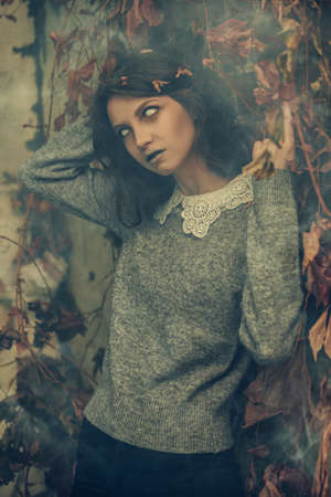 A sad lonely ghost girl with faded eyes and matted black hair stands among withered foliage and looks at the camera. Horror film, thriller. Halloween.の写真素材