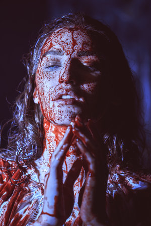 Spooky portrait of a poor innocent girl drenched in blood standing weak in a dark room. Horror, thriller. Halloween. Vampires.の写真素材