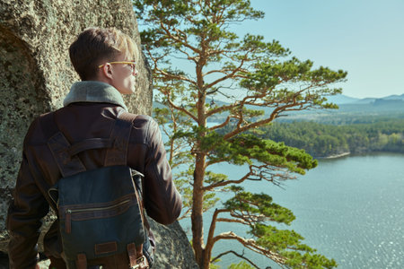 A courageous guy in a leather jacket and with a leather backpack behind his back stands on a...