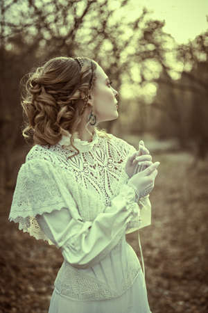 Vintage portrait of a beautiful noble lady in a white dress walking in the old park. Hairstyle and makeup, late 19th century. Historical reconstruction of the Victorian era.の写真素材