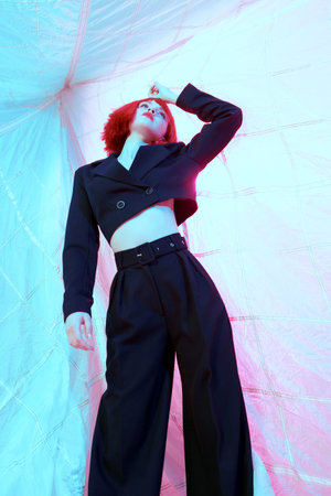 Portrait of an attractive girl model  with bright makeup and trendy red wig posing in a blue...