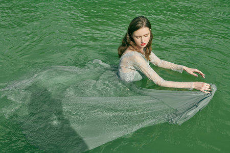 Water nymph. A tender beautiful girl with dark hair in a light flowing dress poses in the water of...