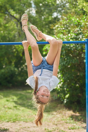Healthy summer holidays. An active girl child is hanging upside down on a horizontal bar in a summer...
