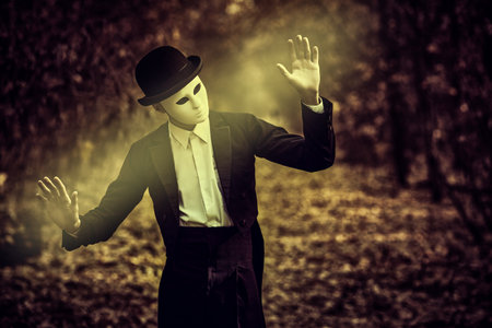 Portrait of a mysterious gentleman in a white carnival mask, bowler hat and black tailcoat standing...
