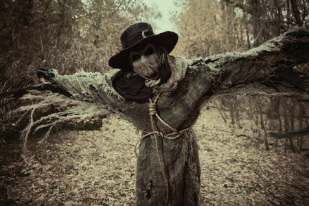 Halloween nightmare. An evil, insidious Scarecrow with a canvas bag on his head, in sackcloth clothes and a black hat, attacks in the dense autumn forest. Horror, thriller.の写真素材