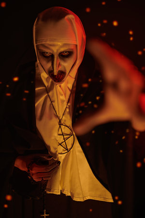 Portrait of an angry devilish nun with bloody teeth surrounded by sparks of hellfire stretching her...