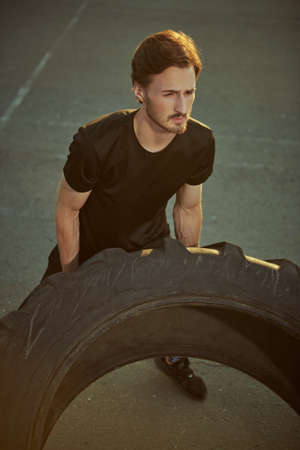 Tire workout outdoors. A sporty guy is doing a tire flip excercise outdoors. Active lifestyle. Sport hobbies.の写真素材