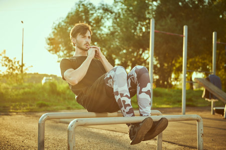Athletic man is doing abdominal exercises on outdoor gym equipment in the park. Sport, fitness,...