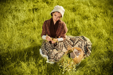 Scottish girl of the 18th century. A medieval rural girl is sitting peacefully on the meadow lit by...