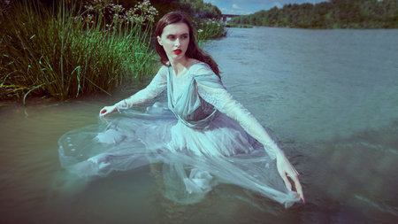 Water nymph. A tender beautiful girl with dark hair in a light flowing dress poses in the water of the lake. Fairytale heroine.の写真素材