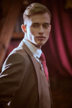 Men's beauty, fashion. Serious young blond man poses in an expensive three-piece suit, white shirt and tie in vintage interior.の写真素材