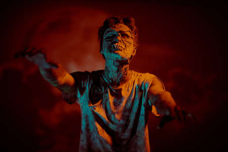 A terrible bloodthirsty zombie stands against the background of a red bloody full moon. The Apocalypse. Halloween, horror movie.の写真素材