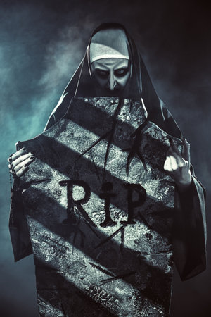 Halloween and Horrors. Devilish evil nun in a cemetery with a tombstone. Mysterious fog around.の写真素材