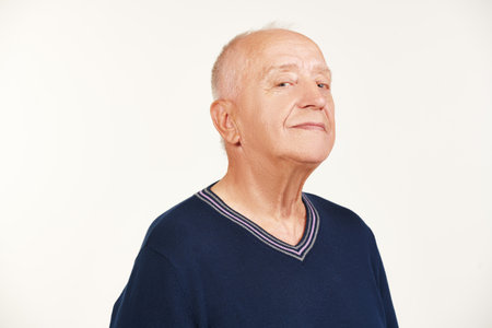 An elderly man in his 70s in modern casual clothes is looking at the camera and smiling. Studio portrait on a white background.の写真素材