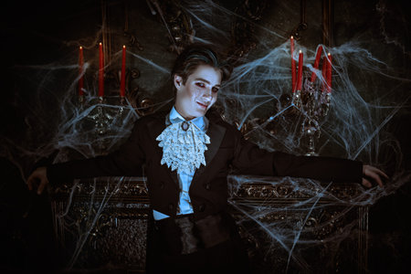 Halloween. An attractive young vampire in an elegant tailcoat stands by the fireplace in an old...