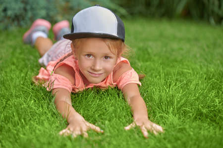 A cute little girl in summer clothes lies on the green lawn outdoors on a sunny day enjoying carefree summertime. Happy summer holidays. Active kids.の写真素材