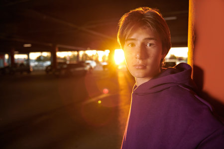 A teenage boy in modern youth clothes walks alone on the backstreet at sunset. Modern generation....