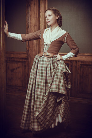 Full length shot of a beautiful aristocratic girl in an 18th century Scottish dress standing in a room with classic vintage interior. The heroine of the novel. 18th century style.の写真素材