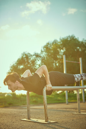 A sporty young man is doing push-up exercises at the gym in the park at sunset. Outdoor sports. Active healthy lifestyle.の写真素材