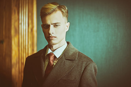 A serious young man in an elegant coat stands in a vintage style apartment. Luxury lifestyle. Men's...