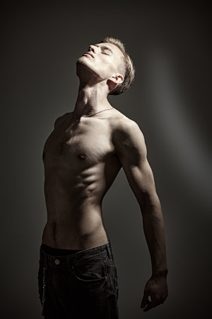 Portrait of a handsome expressive young man with bare torso standing with closed eyes in dark lighting being tortured by his thoughts. Emotions, inner world, psychology.の写真素材