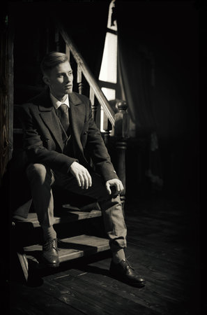A handsome, respectable young man in an expensive coat and three-piece suit sitting on stairs in...