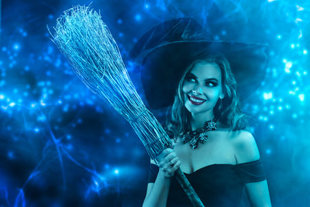 Halloween magic. An attractive girl witch with a broomstick smiles charmingly surrounded by magical...
