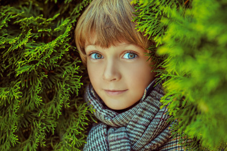 Portrait of a cute blond boy in checkered autumn clothes standing among green bushes. Happy...