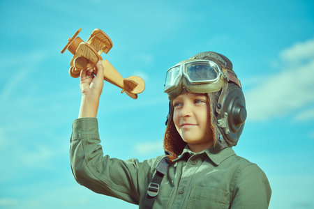 Portrait of a boy in aviator's helmet playing with a toy plane outdoors on a sunny day. Blue sky...