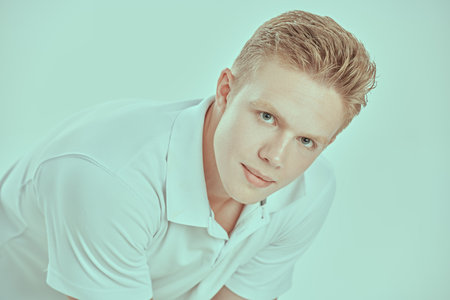 A handsome blond guy in a white polo shirt looks calmly into the camera. White background. Young people concept. Male beauty and health.の写真素材
