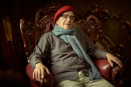 An intelligent elderly man in a beret and glasses rests in a classic vintage armchair at home. Old age.の写真素材