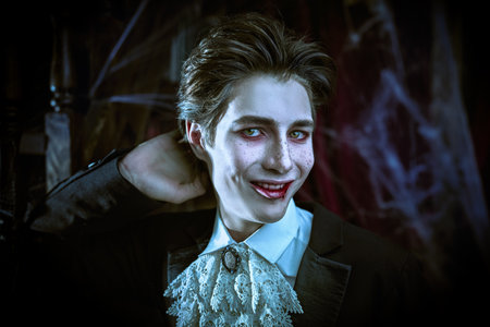 Vampires. Halloween. A comical teenage vampire in an elegant black tailcoat stands in an old abandoned castle and smiles slyly.の写真素材