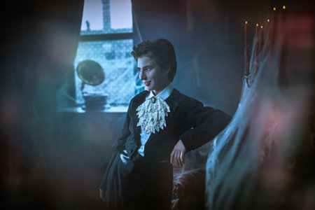 Halloween. An attractive young vampire in an elegant tailcoat stands by the fireplace in an old...