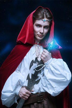 A young prince of elves in a red velvet cloak and a crown stands with a sword in his hands. Starry...