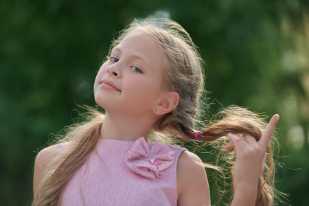 A cute fair-haired girl child with blonde hair wearing a nice summer pink dress walks in a green...