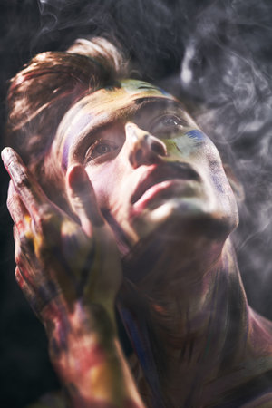 Body painting project. Portrait of a handsome man with colorful painted face on a black background...