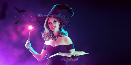 A charming young witch in a black hat casts a spell with a magic wand and a Book of Spells. Dark background with magical pink light and flying bats. Halloween party poster. Copy space.の写真素材