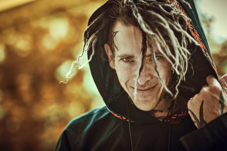Close-up portrait of a brutal mature man with dreadlocks on his head in a black ethnic cloak, who is looking at the camera and smiling. Rock and punk culture.の写真素材