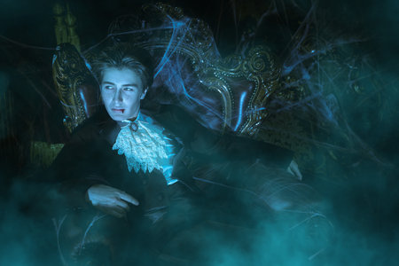 Vampires. A handsome teenage vampire aristocrat sits in a vintage armchair in his old castle, immersed in heavy thoughts. A novel about vampires. Halloween.の写真素材