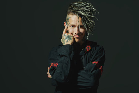 Rock musician. Portrait of a brutal mature man with ethnic tattoos and mohawk dreadlocks on his head posing expressively on a black studio background. Ethnic rock and punk culture.の写真素材