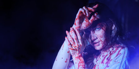 Portrait of a poor innocent girl drenched in blood standing weak in a dark room. Vampires. Horror, thriller. Halloween. Copy space.の写真素材