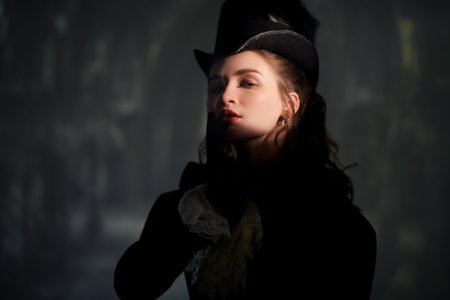 Vintage portrait of a beautiful lady in an elegant dress and a hat standing in the shade of the windows of an old building. Style of the late 19th - early 20th century.の写真素材