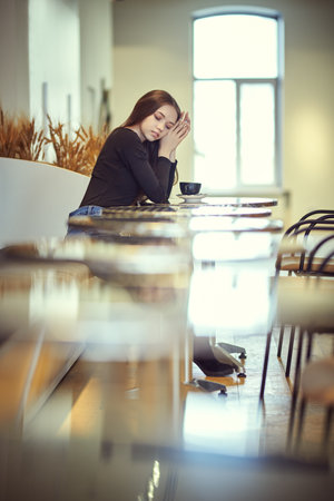 A lovely girl with long brown hair sits at a table in a cafe drinking a cup of tea. People and lifestyle.の写真素材