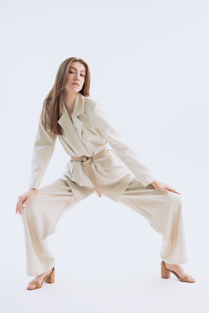 Elegant style. A beautiful fashion model poses in a loose beige pantsuit on a white background. Female fashion. Full-length studio portrait.の写真素材