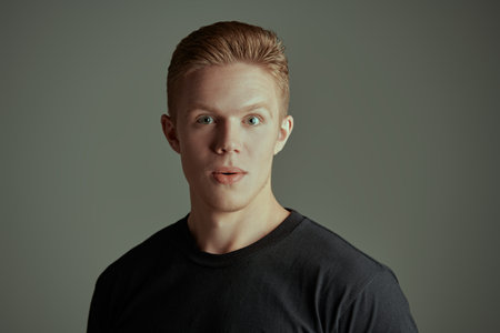 Portrait of a handsome blond guy in a black t-shirt looking with surprise and excitement at the...