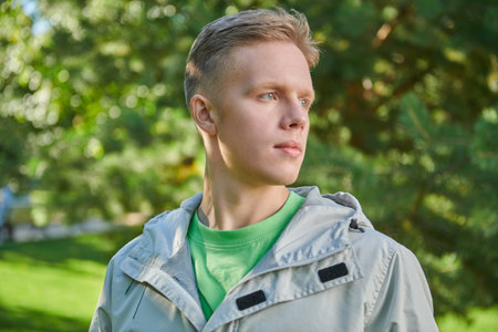 A handsome guy in stylish youth clothes stands in a green sunny park. Young people. Youth fashion.の写真素材