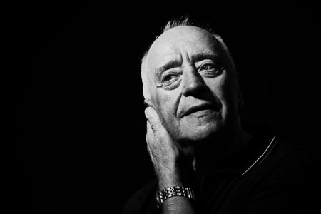 Black and white shot of a calm and thoughtful elderly man in his 70s on a black background. Elderly age. Copy space.の写真素材