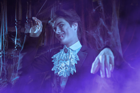 Vampires. Halloween. A comical teenage vampire in an elegant black tailcoat stands in an old abandoned castle and smirks unkindly.の写真素材
